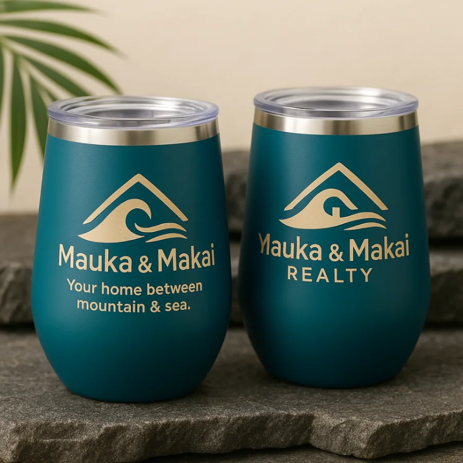 Two teal insulated wine tumblers on lava rock, printed in cream with the Mauka and Makai Realty mark, wordmark and tagline.